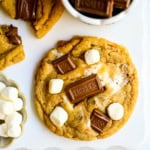 These homemade s'mores cookies are thick, soft, and chewy with gooey marshmallow bits and chopped Hershey bar throughout every bite. A full cup of finely crushed graham cracker crumbs goes straight into the dough, giving these cookies that unmistakable campfire s'mores flavor! This easy s'mores cookie recipe comes together in one bowl and is ready from start to finish in about 30 minutes.