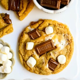 These homemade s'mores cookies are thick, soft, and chewy with gooey marshmallow bits and chopped Hershey bar throughout every bite. A full cup of finely crushed graham cracker crumbs goes straight into the dough, giving these cookies that unmistakable campfire s'mores flavor! This easy s'mores cookie recipe comes together in one bowl and is ready from start to finish in about 30 minutes.