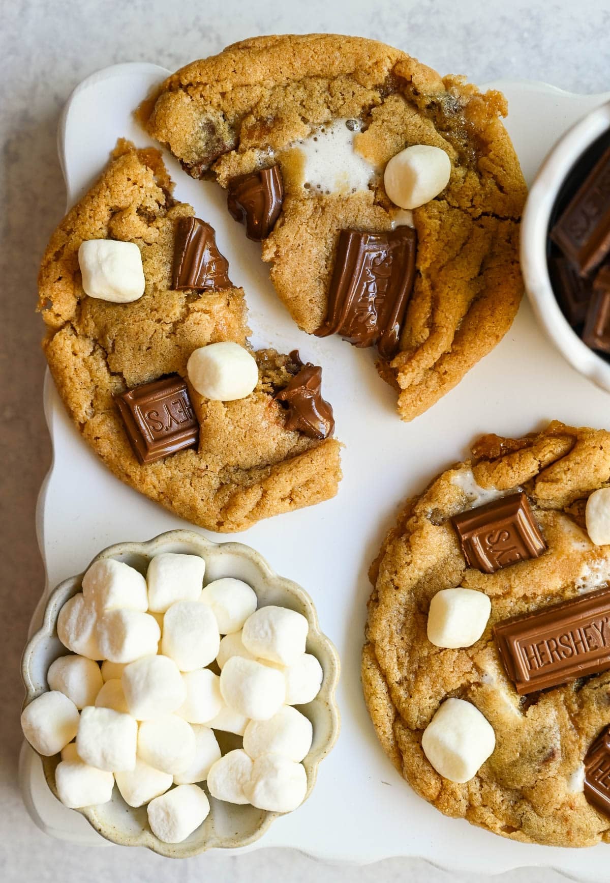These homemade s'mores cookies are thick, soft, and chewy with gooey marshmallow bits and chopped Hershey bar throughout every bite. A full cup of finely crushed graham cracker crumbs goes straight into the dough, giving these cookies that unmistakable campfire s'mores flavor! This easy s'mores cookie recipe comes together in one bowl and is ready from start to finish in about 30 minutes.