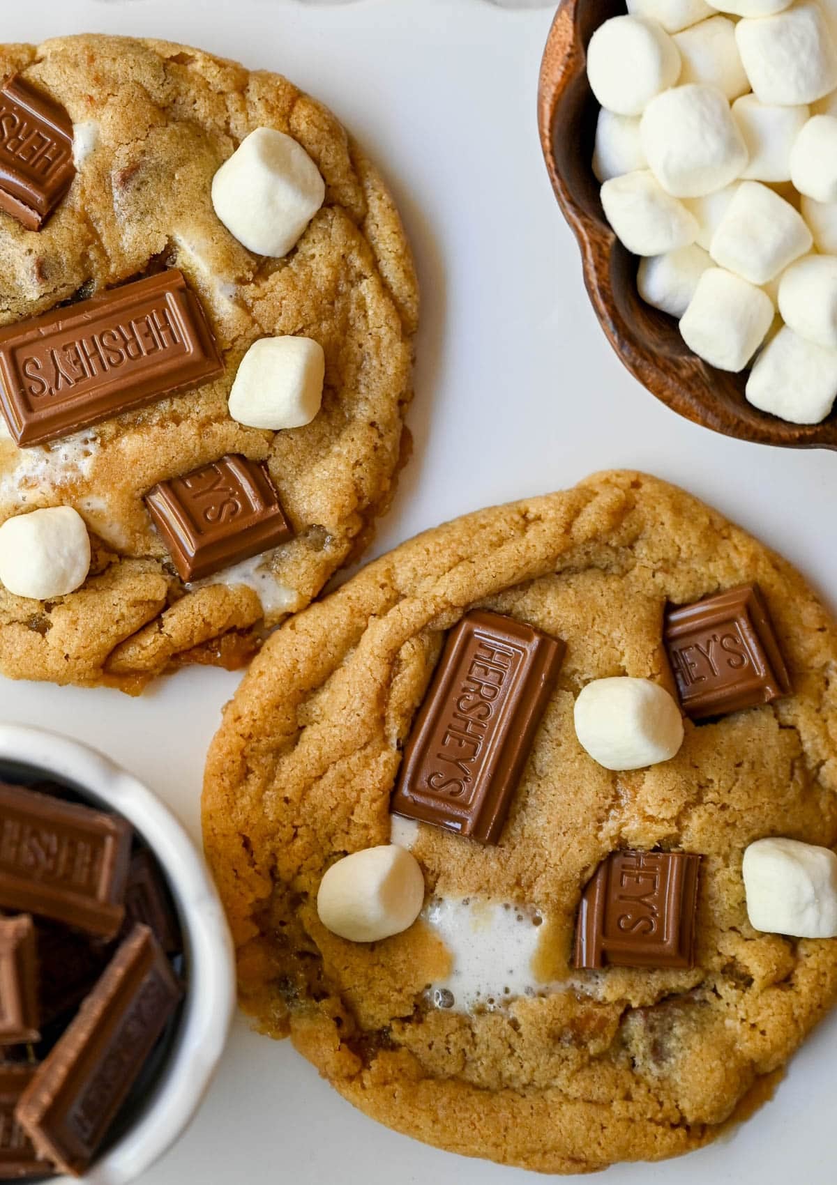 These homemade s'mores cookies are thick, soft, and chewy with gooey marshmallow bits and chopped Hershey bar throughout every bite. A full cup of finely crushed graham cracker crumbs goes straight into the dough, giving these cookies that unmistakable campfire s'mores flavor! This easy s'mores cookie recipe comes together in one bowl and is ready from start to finish in about 30 minutes.