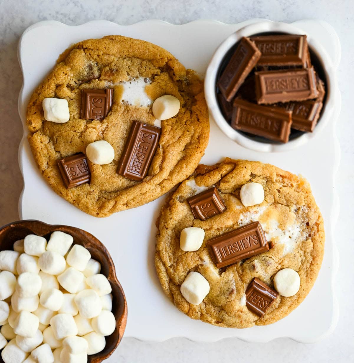 These homemade s'mores cookies are thick, soft, and chewy with gooey marshmallow bits and chopped Hershey bar throughout every bite. A full cup of finely crushed graham cracker crumbs goes straight into the dough, giving these cookies that unmistakable campfire s'mores flavor! This easy s'mores cookie recipe comes together in one bowl and is ready from start to finish in about 30 minutes.