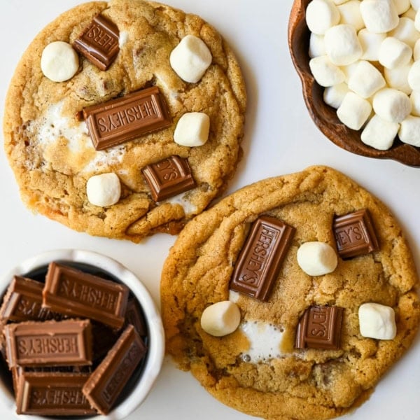 These homemade s'mores cookies are thick, soft, and chewy with gooey marshmallow bits and chopped Hershey bar throughout every bite. A full cup of finely crushed graham cracker crumbs goes straight into the dough, giving these cookies that unmistakable campfire s'mores flavor! This easy s'mores cookie recipe comes together in one bowl and is ready from start to finish in about 30 minutes.