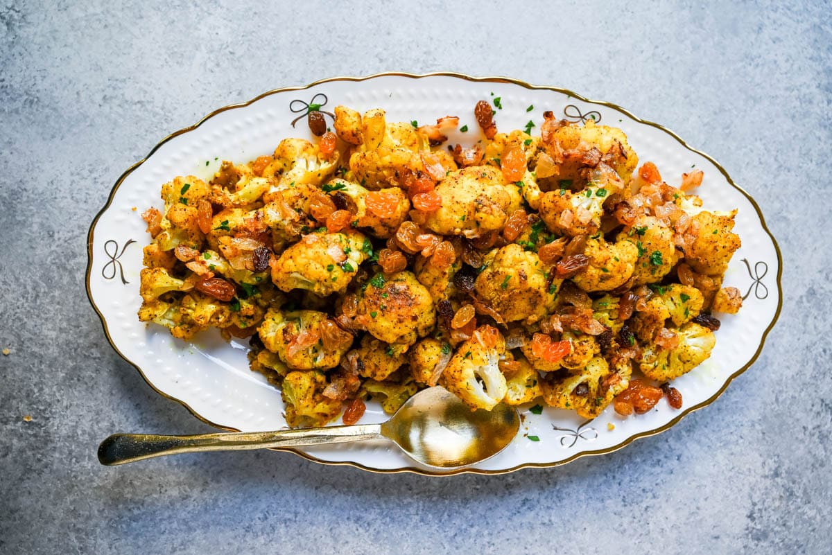 Indian Roasted Cauliflower with Golden Raisins and Pine Nuts. Golden, tender turmeric and curry roasted cauliflower tossed with sweet caramelized onion, golden raisins, and pine nuts. An easy vegan-friendly side.