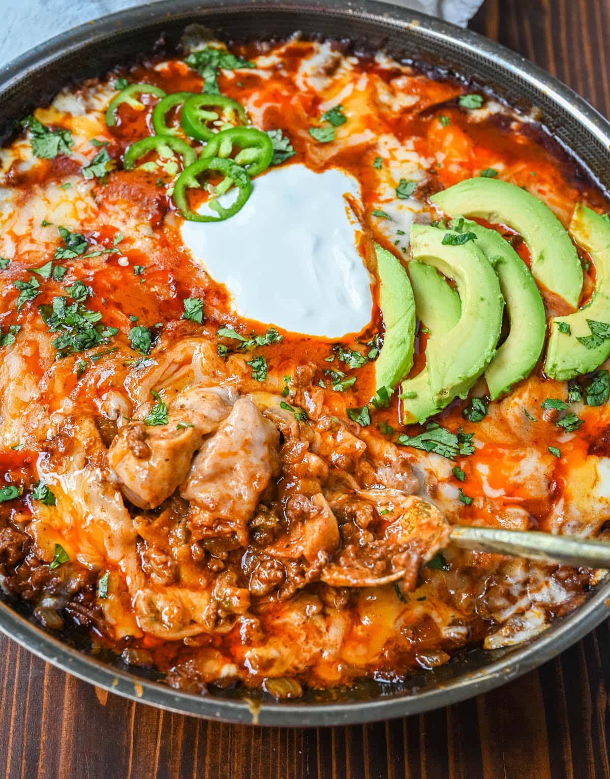 Beef Enchiladas in a skillet topped with sour cream, avocado, and cilantro. Easy ground beef enchilada skillet recipe.