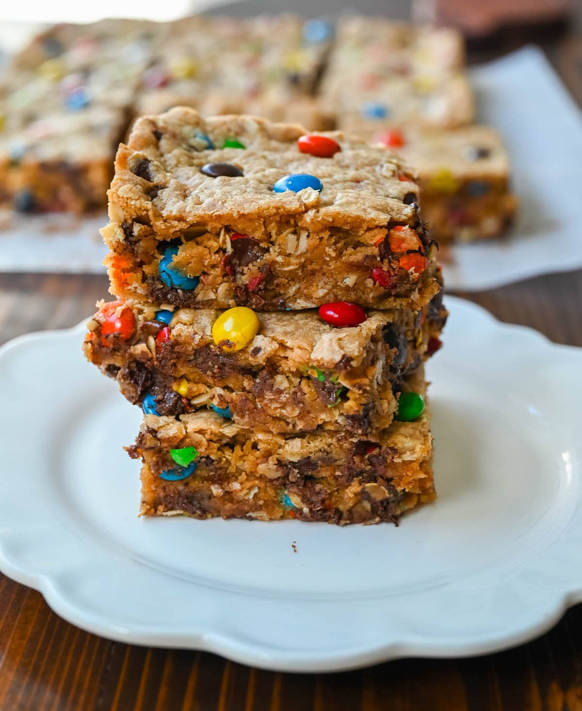 Monster cookie bars stacked. These Monster Cookie Bars are thick, chewy peanut butter oatmeal bars loaded with M&M’s and chocolate chips. One bowl, one 9x13 pan, and no scooping! How to make the best monster cookie bars.